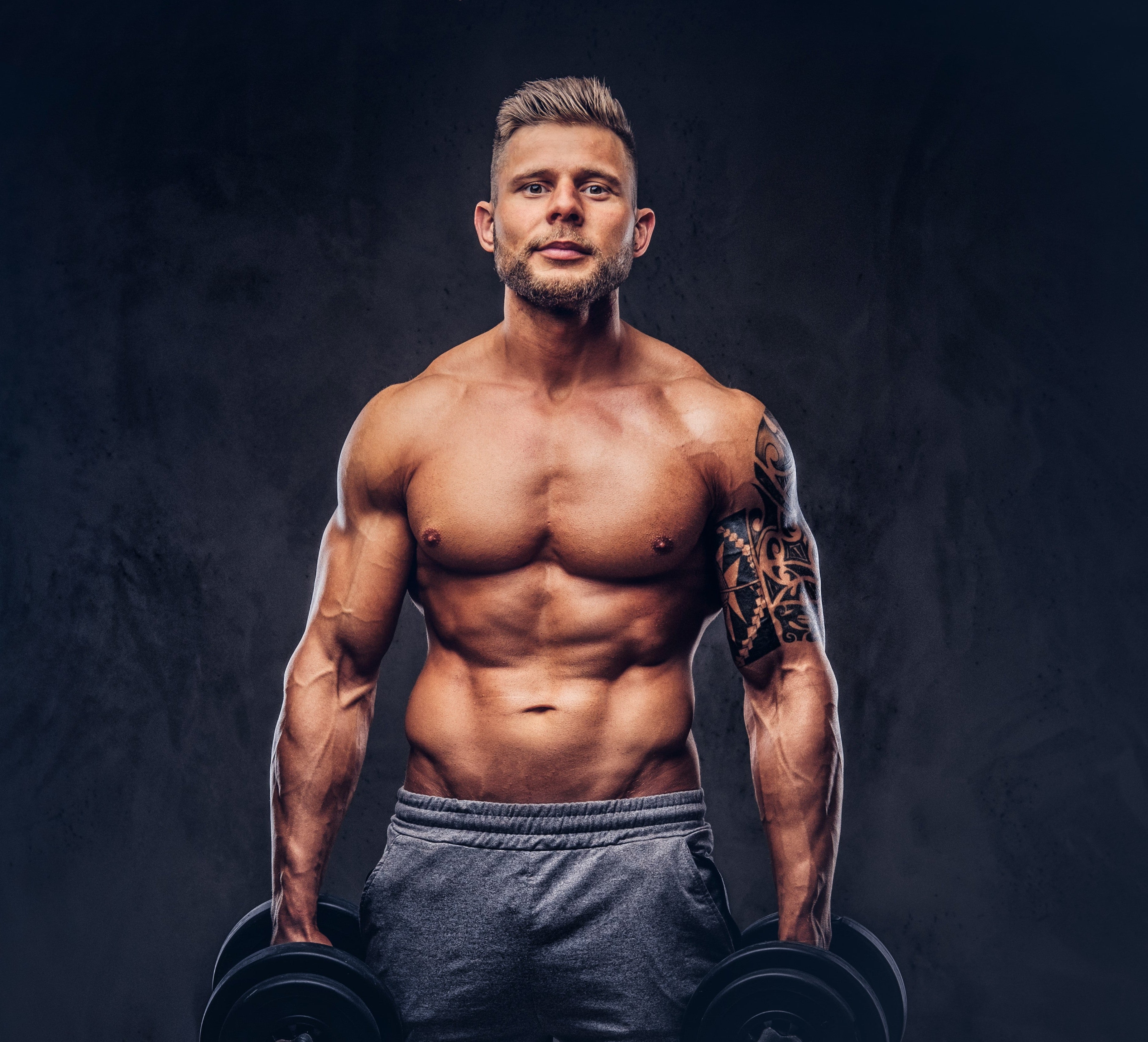 potente-culturista-elegante-con-tatuaje-en-el-brazo-posando-con-pesas-en-un-estudio-aislado-en-un-fondo-oscuro_a83f7a5a-0594-4ee0-b5d7-cd534ab2d0d7.jpg